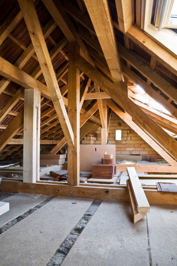 Grenier en rénovation avec charpente bois apparente, poutres neuves, tuiles, fenêtre de toit et isolation en cours. Matériaux de construction visibles.